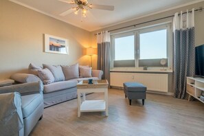 Ein Wohnzimmer mit einer Couch, einem Couchtisch, einem Fernseher und einem Fenster mit Vorhängen.
