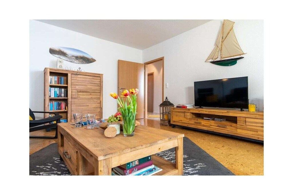 Ein Wohnzimmer mit Couchtisch aus Holz, Bücherregal, Fernseher und einer Segelboot-Dekoration an der Wand.