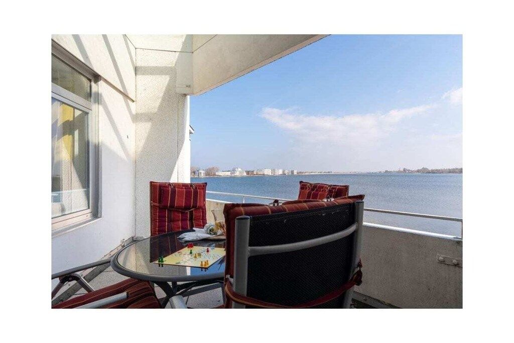 Un balcon avec une table et des chaises, une vue sur l’eau et un panorama sur la ville au loin.
