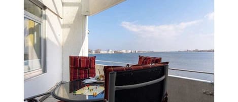 Un balcon avec une table et des chaises, une vue sur l’eau et un panorama sur la ville au loin.