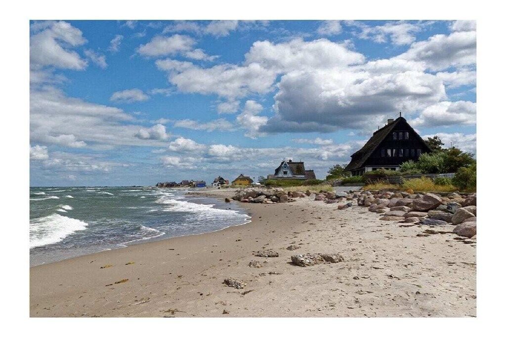 Une plage bordée d’une rangée de maisons, dont certaines sont coiffées de toits de chaume, et un rivage rocheux.