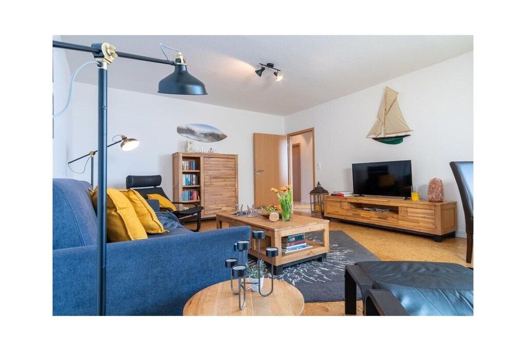 Una sala de estar con sofá, mesa de centro, televisor, estantería y una decoración náutica con un velero.