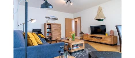 Una sala de estar con sofá, mesa de centro, televisor, estantería y una decoración náutica con un velero.