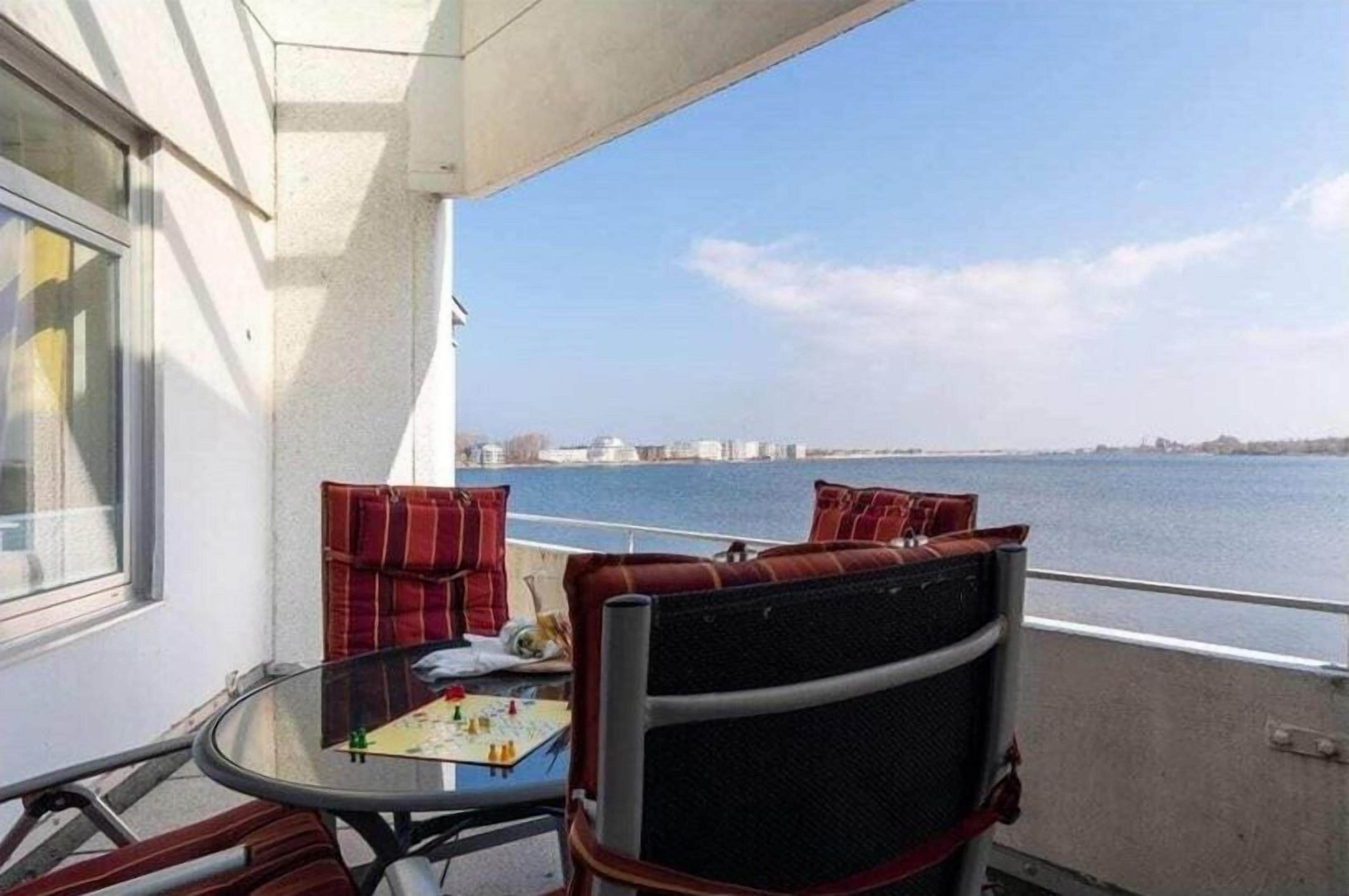 A balcony with a table and chairs, a view of the water, and a distant cityscape.