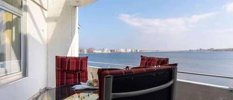A balcony with a table and chairs, a view of the water, and a distant cityscape.