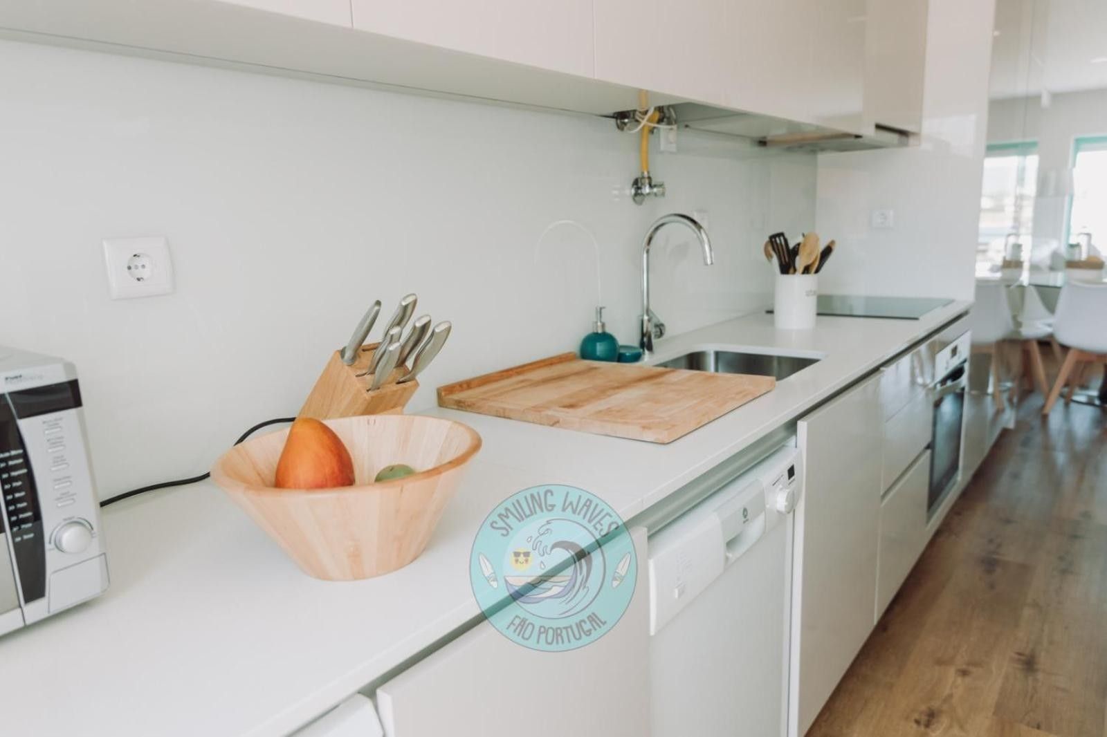 A modern kitchen with a white countertop, a wooden cutting board, a bowl, and a knife block.