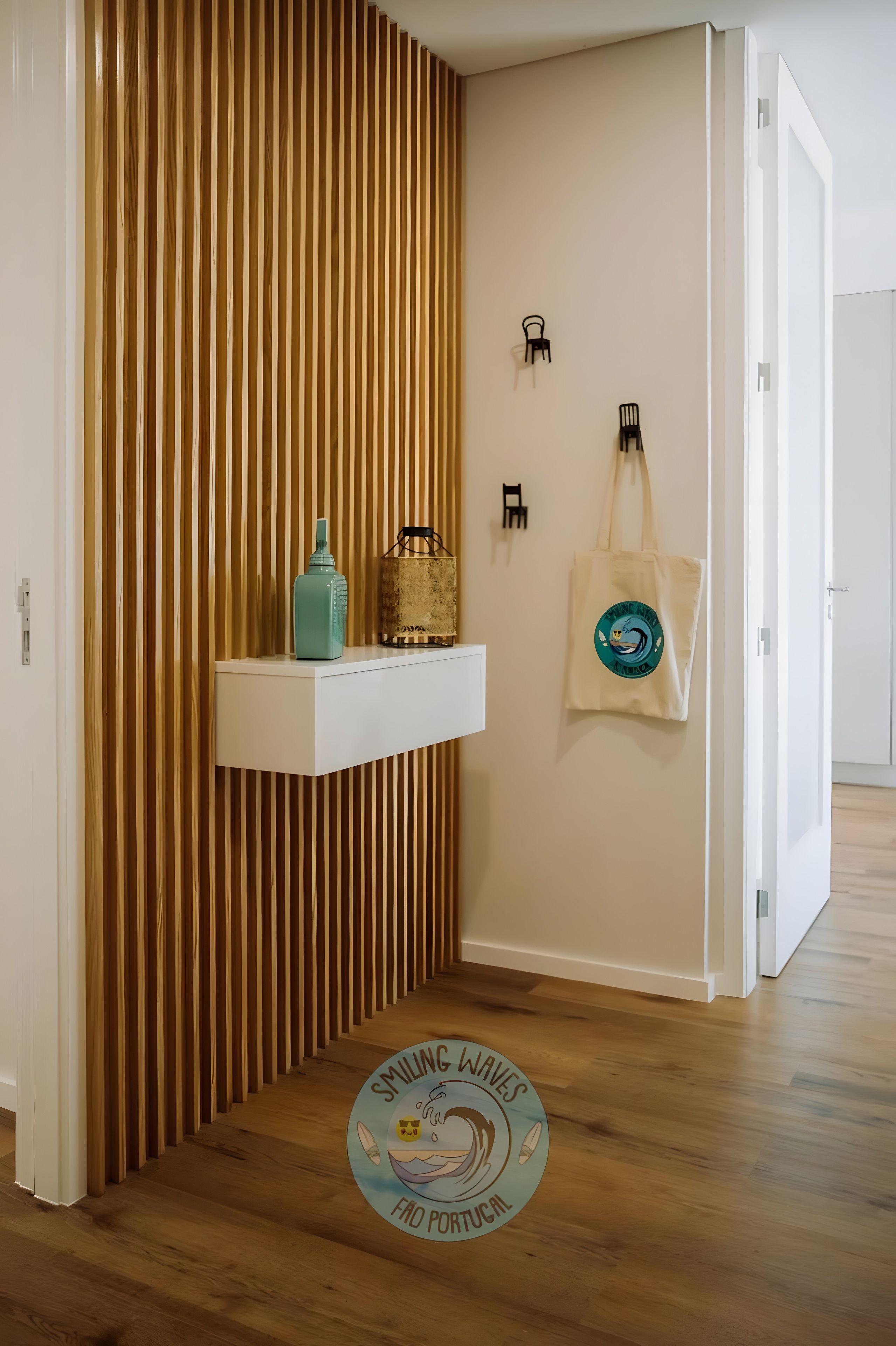 Un couloir avec un mur lambrissé en bois, une étagère blanche sur laquelle se trouve une bouteille turquoise, un panier tressé et un sac fourre-tout orné d’un logo.