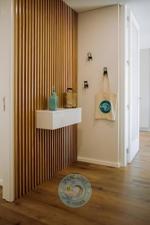 A hallway with a wooden slat wall, a white shelf with a teal bottle, a woven basket, and a tote bag with a logo.