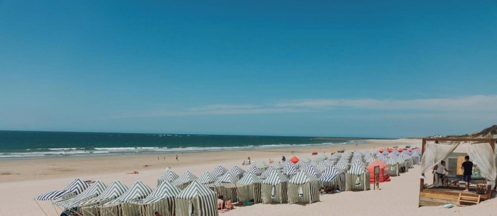 Ein Strand mit Reihen von gestreiften Sonnenschirmen und einigen Strandkörben.
