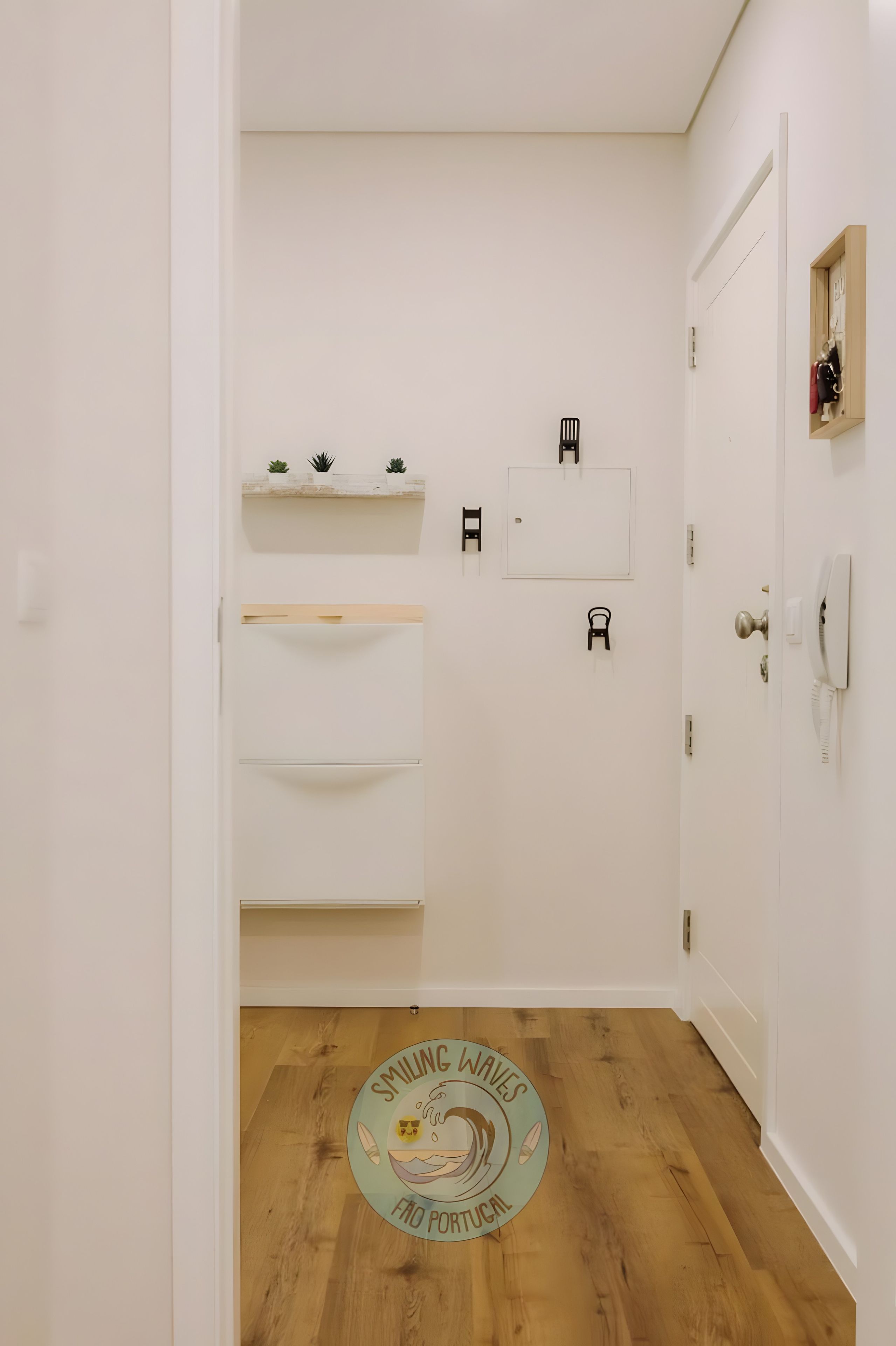 Ein schlichtes Badezimmer mit weißen Wänden, Holzboden und einer Tür, über der sich eine kleine Holzablage befindet.