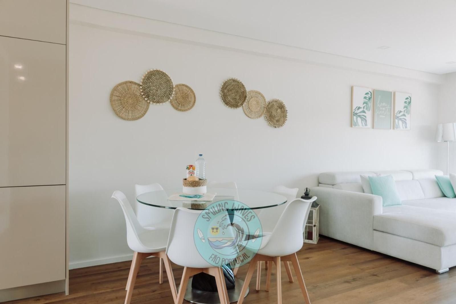 Un salon moderne avec une table à manger en verre, des chaises blanches, un canapé blanc et des œuvres d’art décoratives au mur.