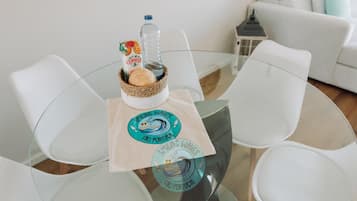 Une table ronde en verre sur laquelle repose un panier tressé contenant une bouteille et une boîte, ainsi que deux sets de table ornés d’un logo.