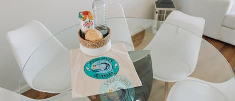 A round glass table with a woven basket containing a bottle and a box, and two placemats with a logo.