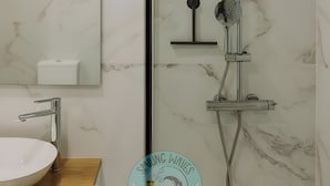 Ein Badezimmer mit weißer Marmorwand, einem Waschbecken mit Holztischplatte, einem Spiegel und einer Dusche inklusive Handbrause.