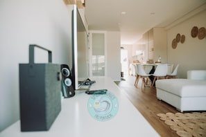 A modern living room with a white sofa, a dining area with white chairs, and a kitchen in the background.