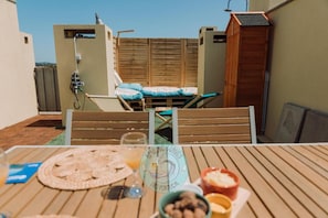 Une terrasse sur le toit, avec une table dressée pour le dîner, une plateforme en bois et une vue sur les environs.