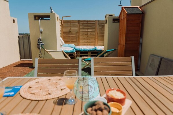 A rooftop terrace with a table set for dining, a wooden deck, and a view of the surrounding area.