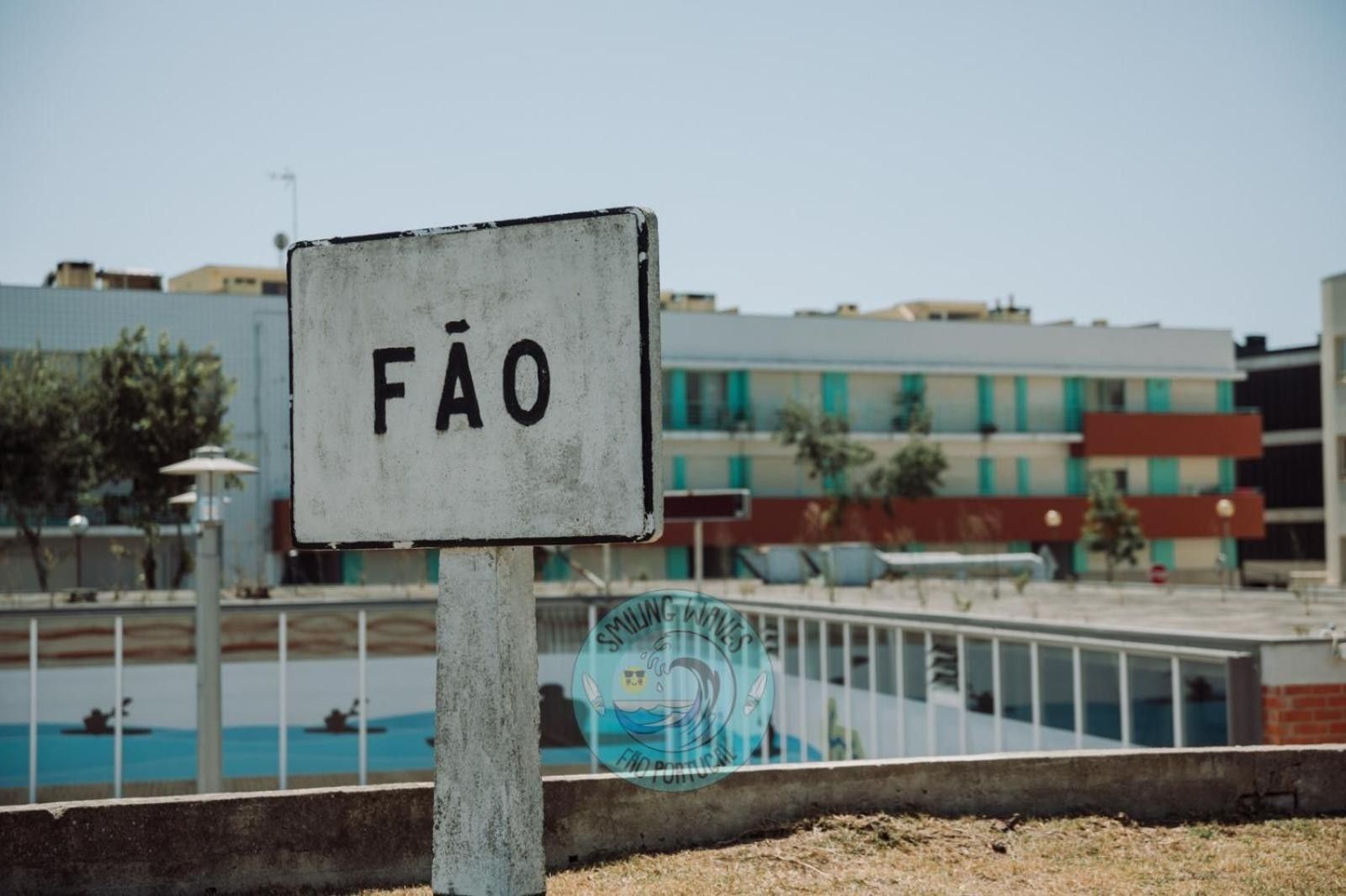 Ein Schild mit dem Wort 'FÃO' an einem Pfosten in der Nähe einer Uferpromenade, im Hintergrund Gebäude.