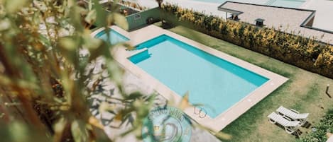 A swimming pool with a surrounding lawn and a few lounge chairs.