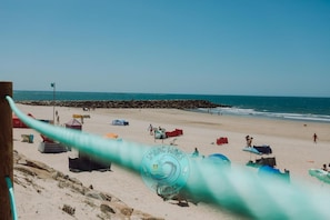 Une plage avec un ciel dégagé, une digue rocheuse et un espace aménagé avec des tentes.