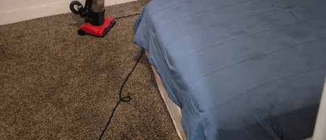 A room with a single bed, a vacuum cleaner, and a wall socket.