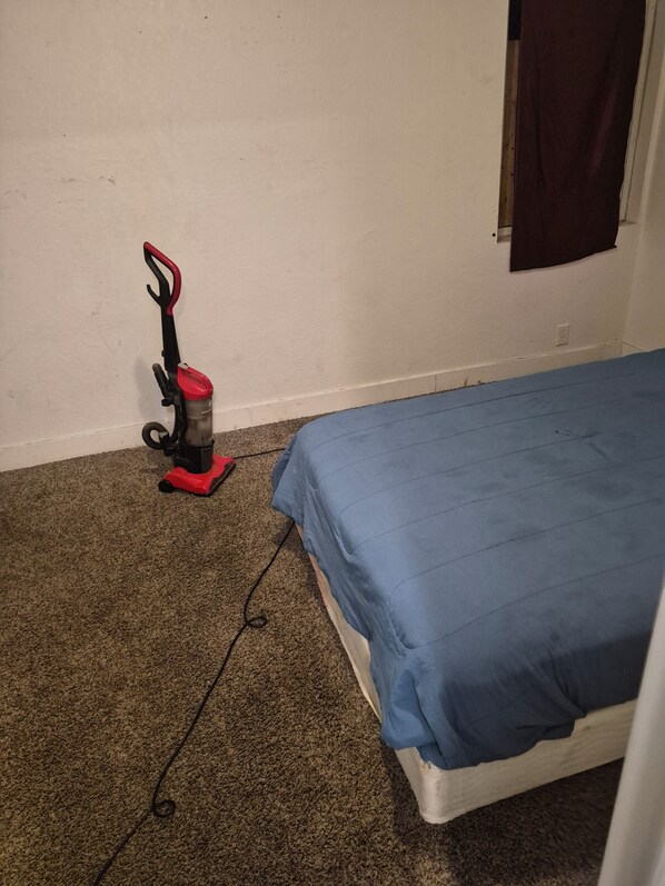 A room with a single bed, a vacuum cleaner, and a wall socket.