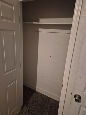 A white door with a metal handle, leading to a room with a carpeted floor and a white wall.