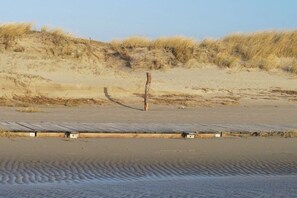 A sandy beach with a wooden boardwalk and dunes in the background. - Friesenhof "Dreilanden" - Kiek mol ut (Sankt Peter-Ording)