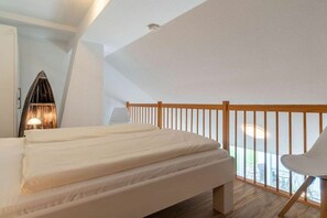A bedroom with a bed, a chair, and a balcony with a railing. - Friesenhof "Dreilanden" - Kiek mol ut (Sankt Peter-Ording)
