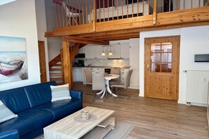 A modern interior with a blue sofa, wooden staircase, kitchen, and dining area. - Friesenhof "Dreilanden" - Kiek mol ut (Sankt Peter-Ording)