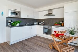 Eine moderne Küche mit weißen Schränken, einer Mikrowelle, einem Backofen und einem Holzwagen mit Lebensmitteln.