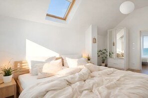 Ein Schlafzimmer mit Oberlicht, einem Bett mit weißer Bettwäsche, einem Nachttisch mit Pflanze und einem weißen Kleiderschrank.
