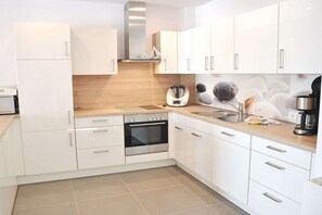 A modern kitchen with white cabinetry, a built-in oven, a coffee maker, and a sink.