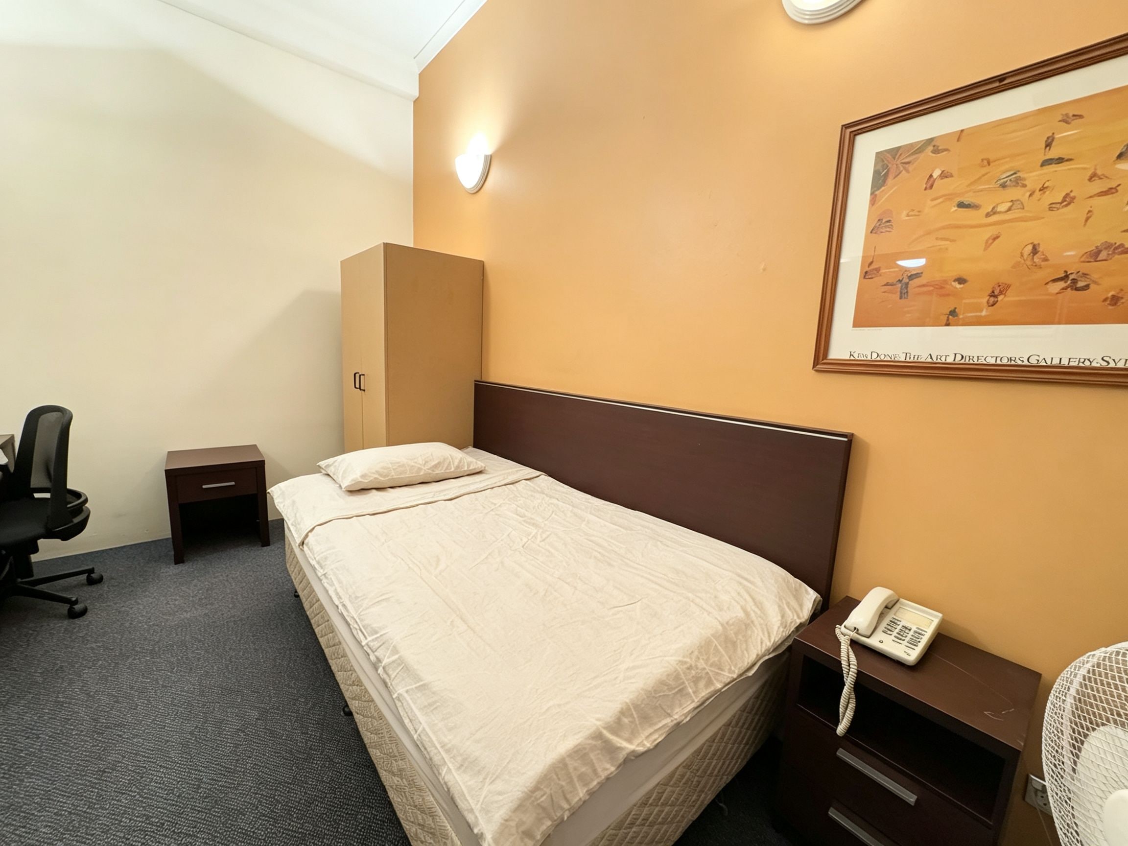 A hotel room with a bed, a desk, a chair, a telephone, and a painting on the wall.
