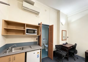 A compact hotel room with a kitchenette, a microwave, a small refrigerator, a desk with a chair, and a toilet visible through an open door. - Modern Studio | Central Ultimo Broadway | Shared Kitchen & Laundry (Ultimo)