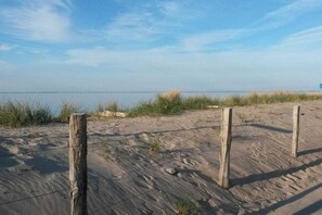 Een zandstrand met houten palen en prikkeldraad omheining.