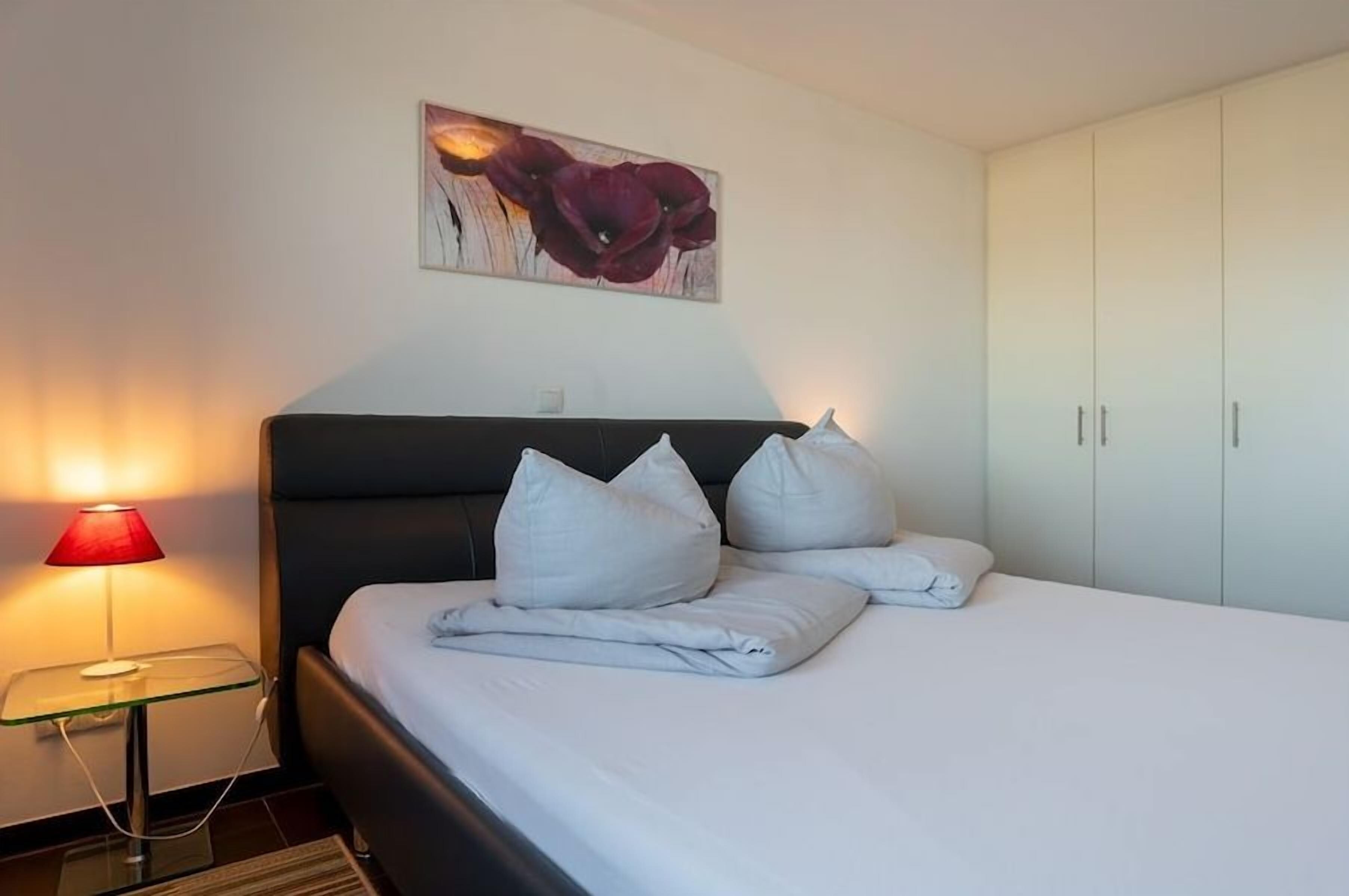 A hotel room with a bed, a bedside lamp, a painting, and a wardrobe.