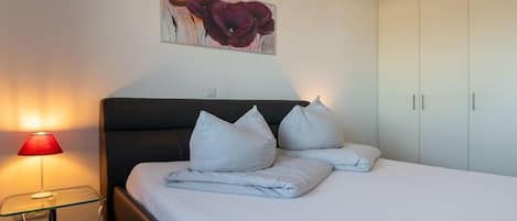 Una habitación de hotel con cama, lámpara de noche, un cuadro y un armario.