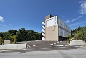 A modern building with a prominent 'S' logo, likely a hotel, with a parking lot in front. - Smile Smart Inn Okinawa Churaumi (Motobu, Kunigami District)
