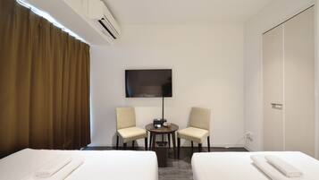 A hotel room with two beds, a TV, and a desk with chairs.