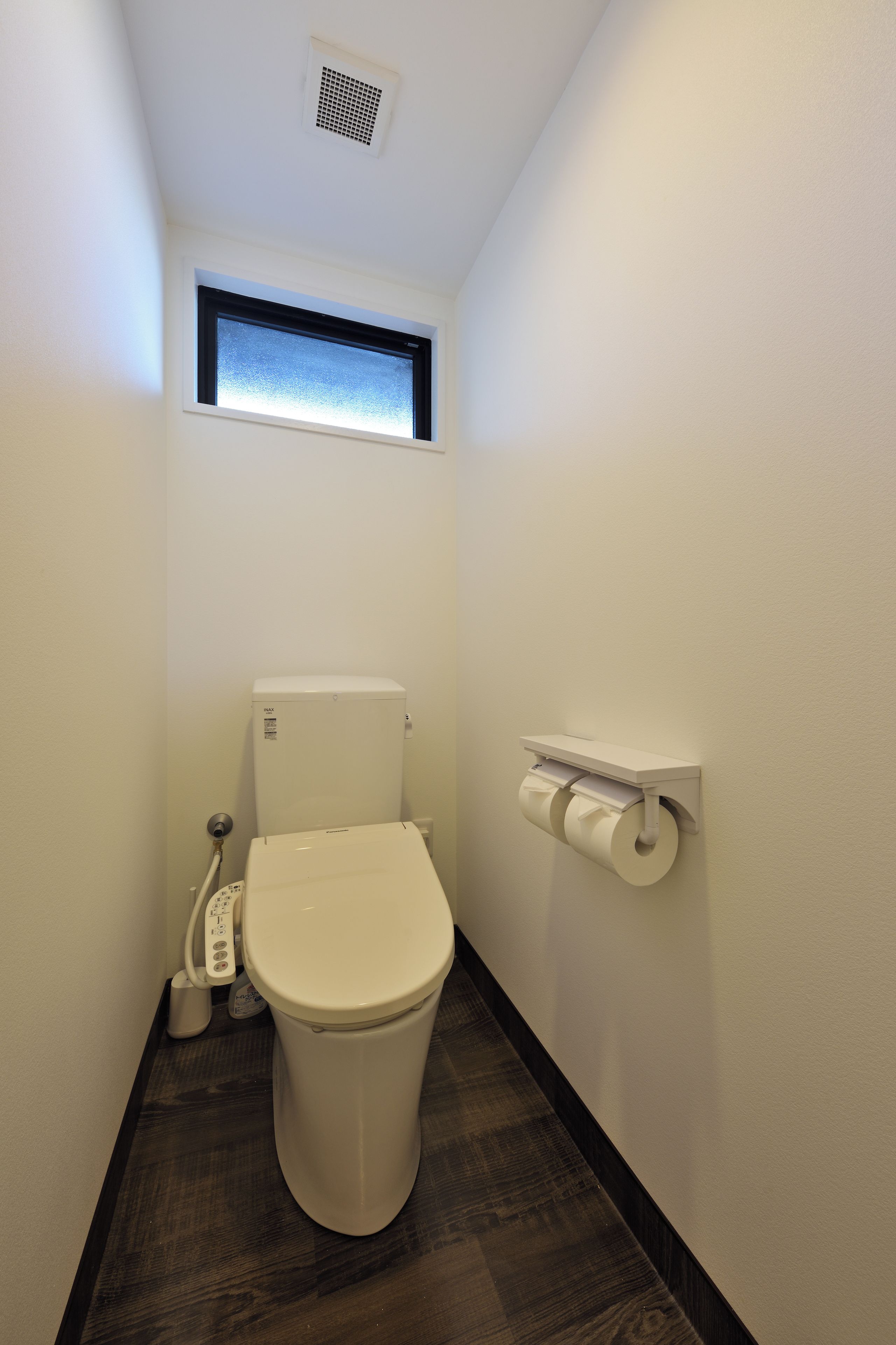 A small, narrow bathroom with a toilet, a window, and a toilet paper holder.