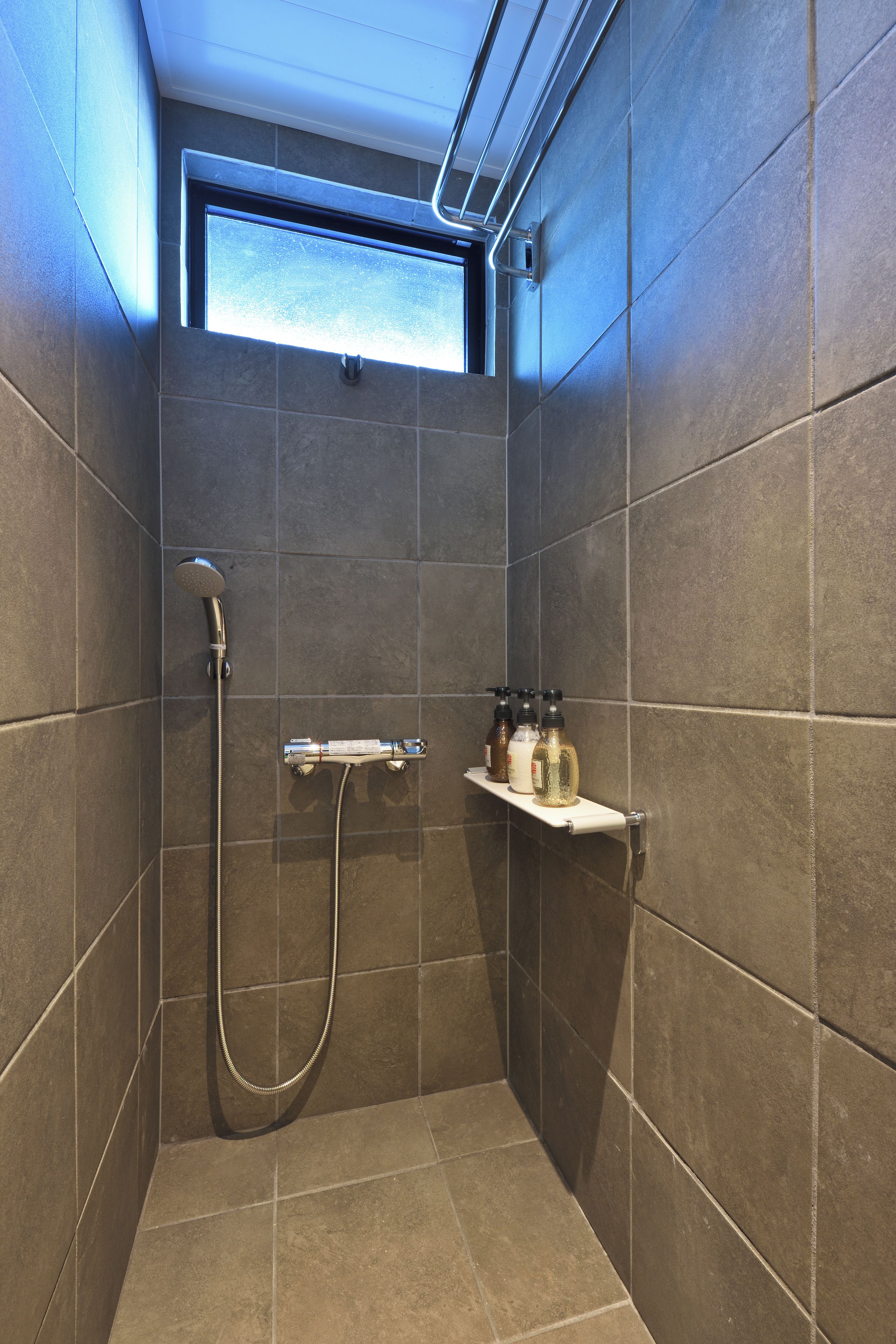 A shower area with a handheld showerhead, a wall-mounted towel rack, and a shelf with toiletries.