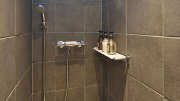 A shower area with a handheld showerhead, a wall-mounted towel rack, and a shelf with toiletries.
