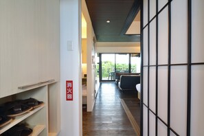 A hallway with a shoe rack, a sign indicating a fire alarm, and a view of a seating area with a table and chairs. - Smile Smart Inn Okinawa Churaumi (Motobu, Kunigami District)