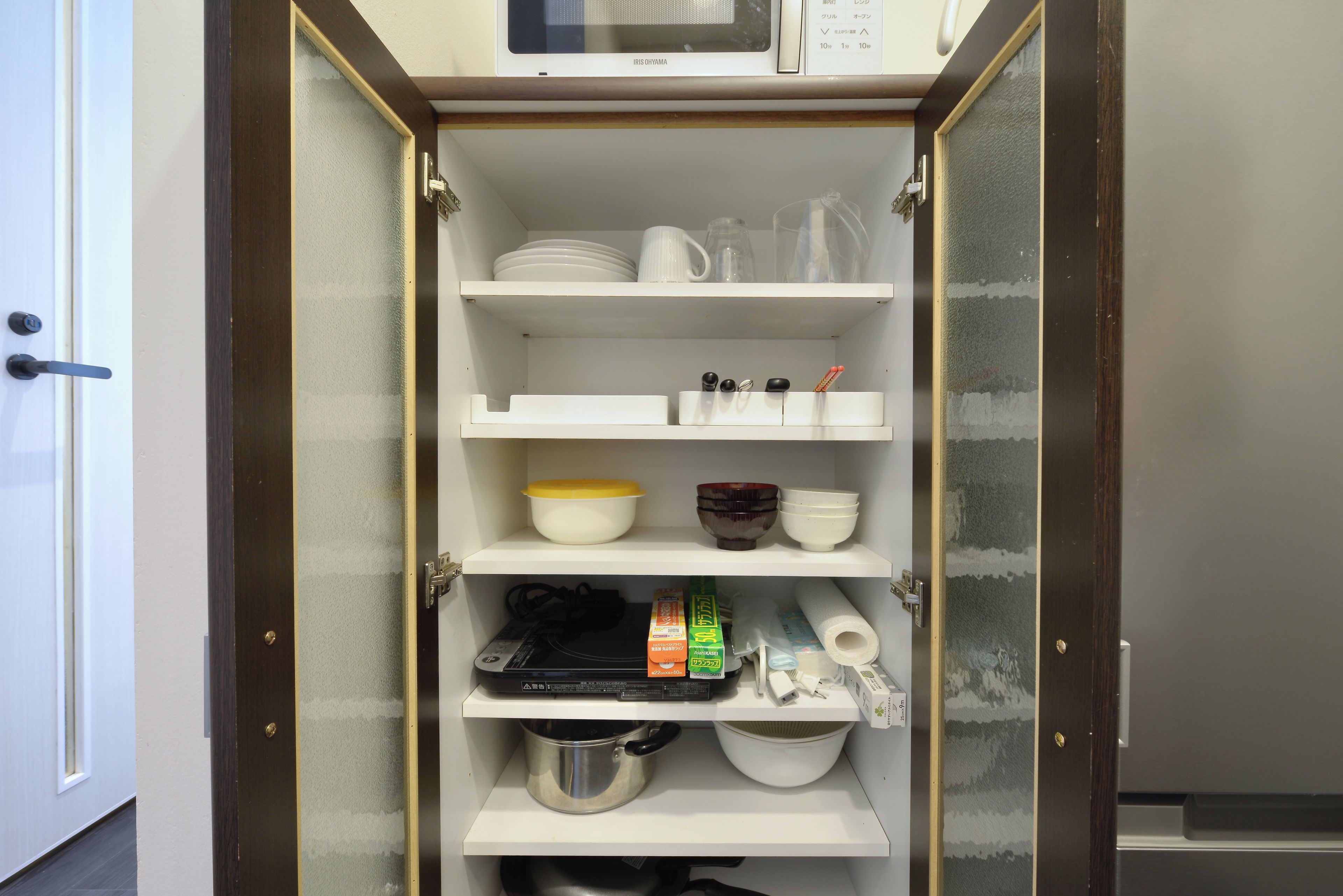 A kitchen pantry with shelves containing dishes, a microwave, and kitchen utensils.