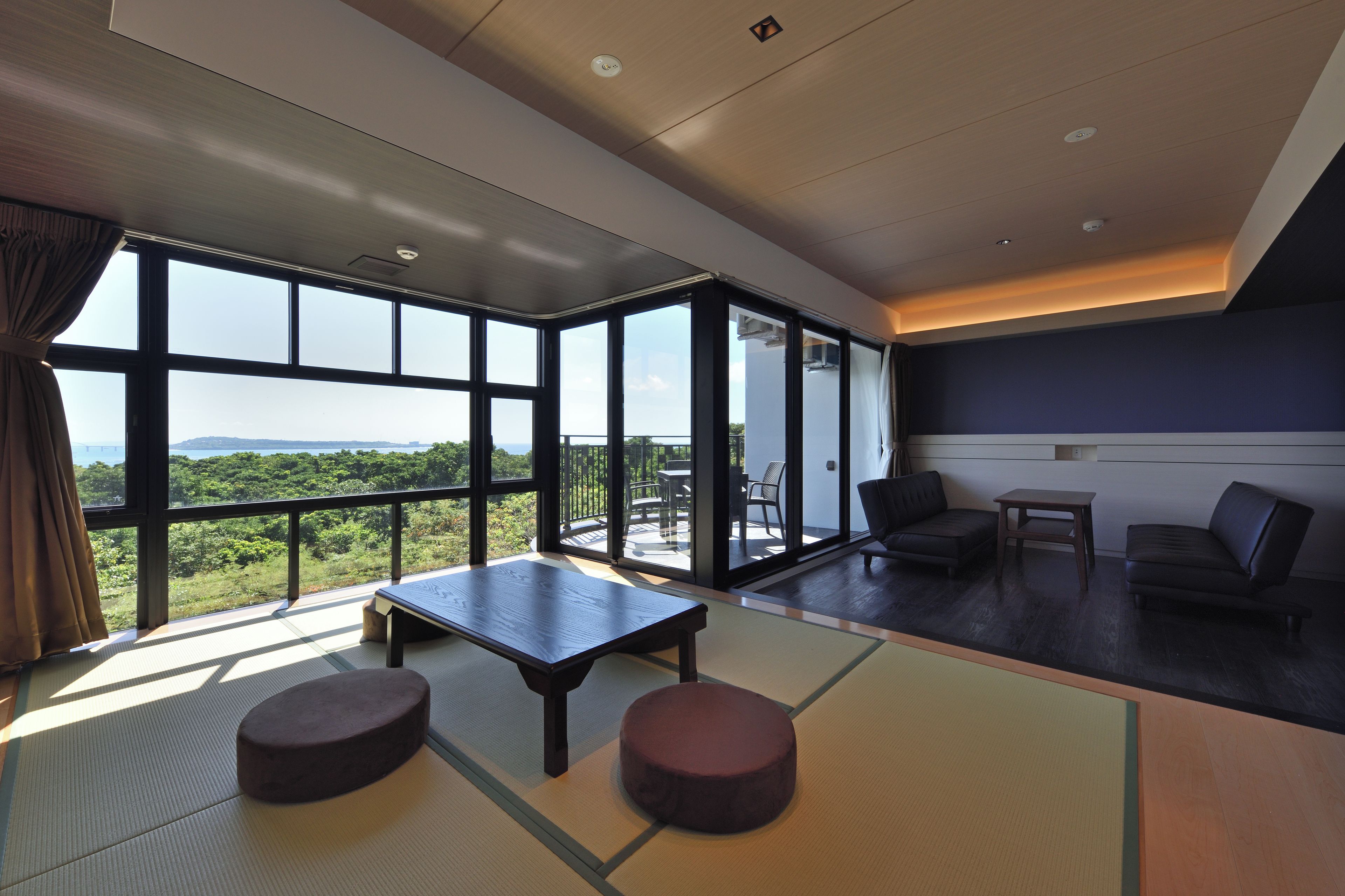 Ein modernes Interieur mit großen Fenstern, einer Zone mit Tatami-Matten und einer Sitzgruppe.