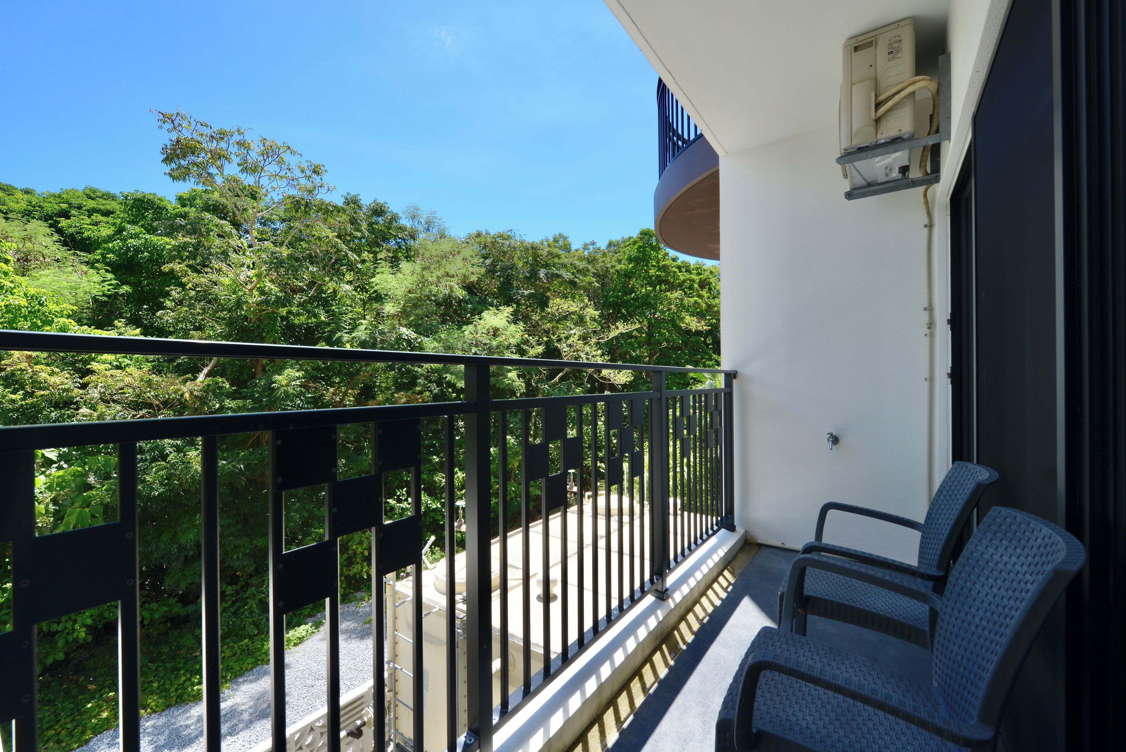 A balcony with a black metal railing, two chairs, and a view of a green landscape.