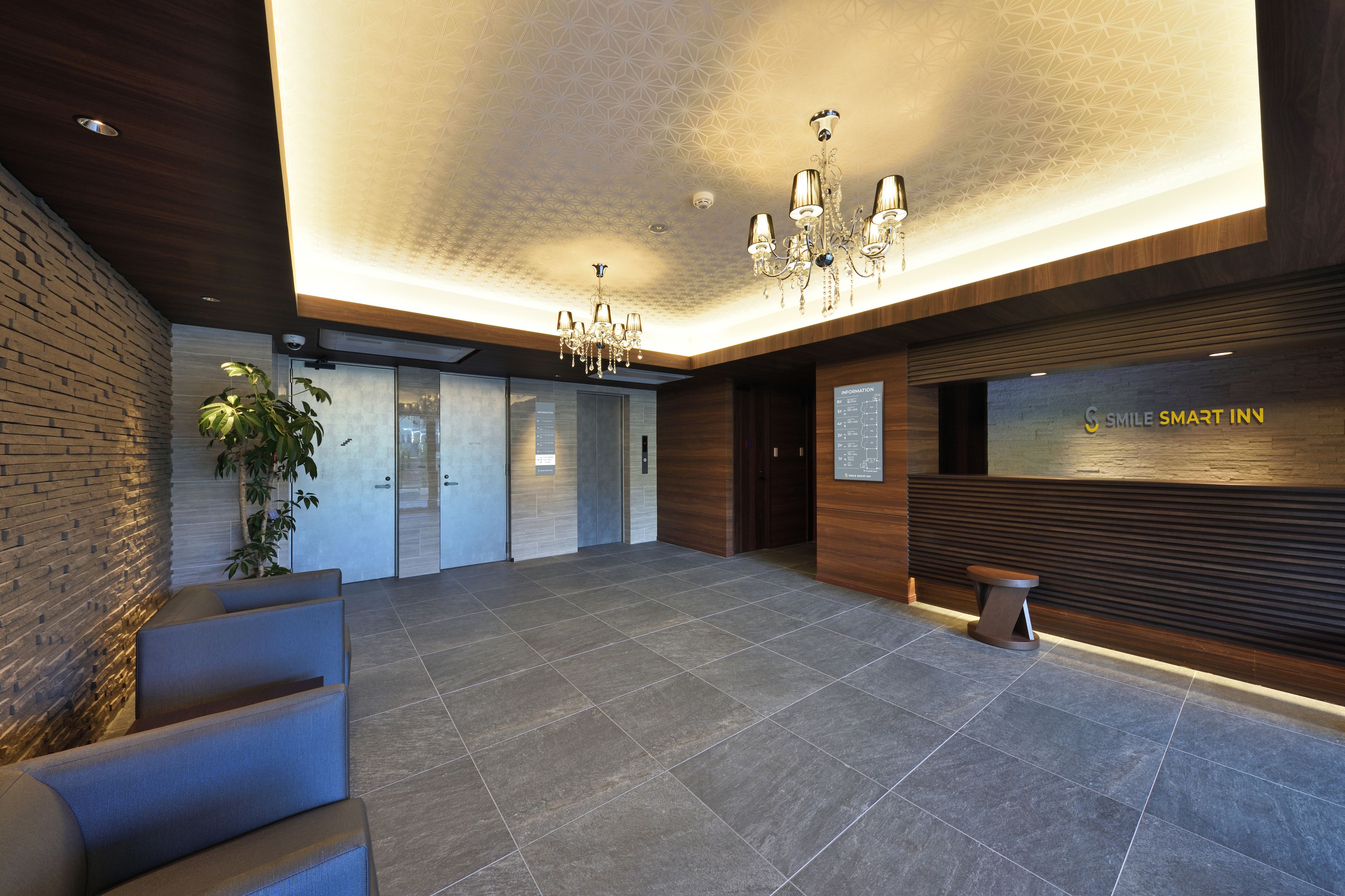 A modern hotel lobby with a reception desk, seating area, and a chandelier.