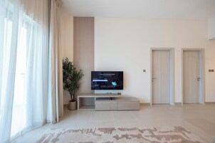 Una sala moderna con un televisor de pantalla plana sobre un mueble bajo, una planta en maceta y un amplio ventanal con cortinas.