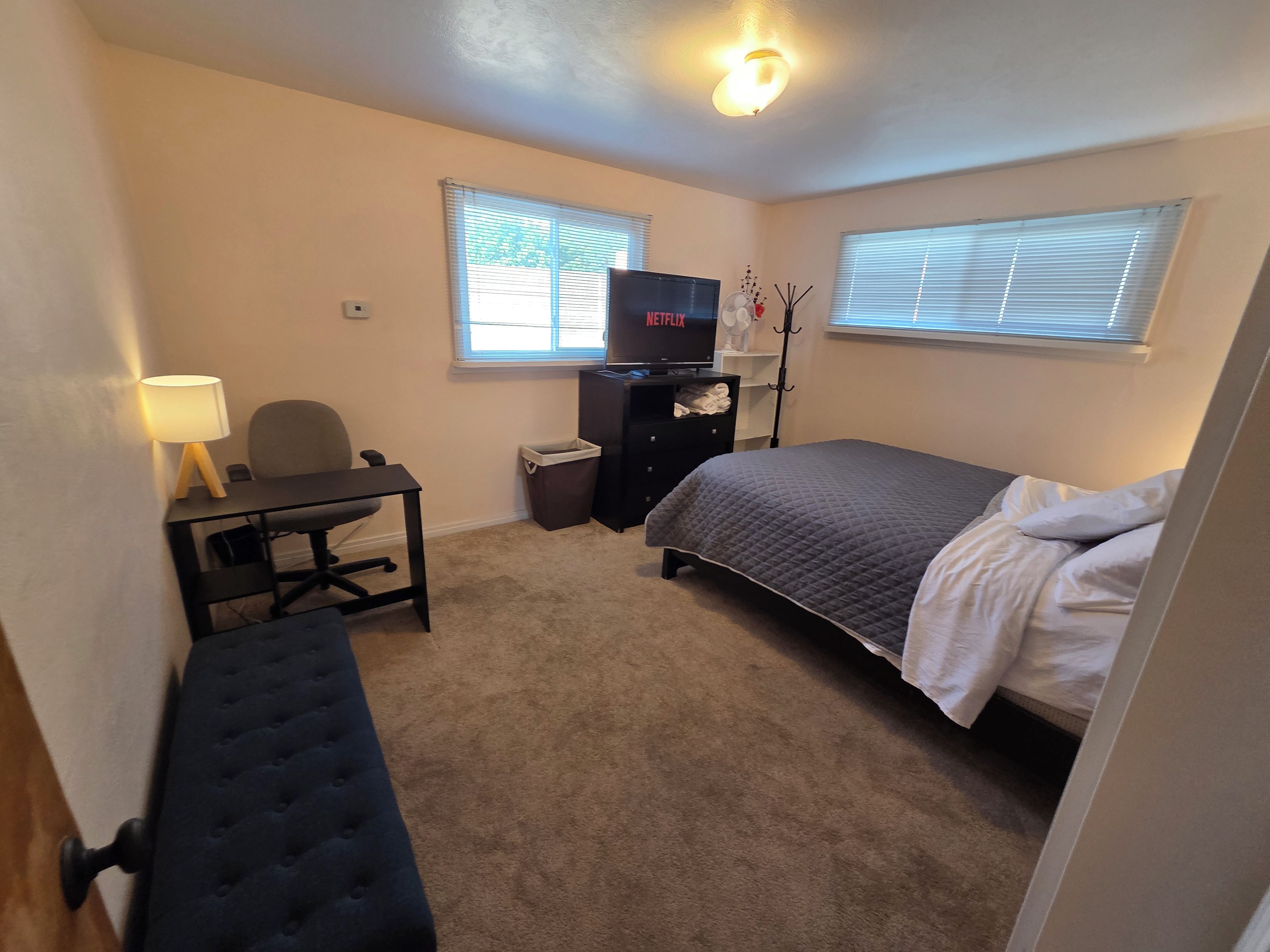 Ein Schlafzimmer mit Bett, Schreibtisch, Stuhl, Fernseher und Fenster.